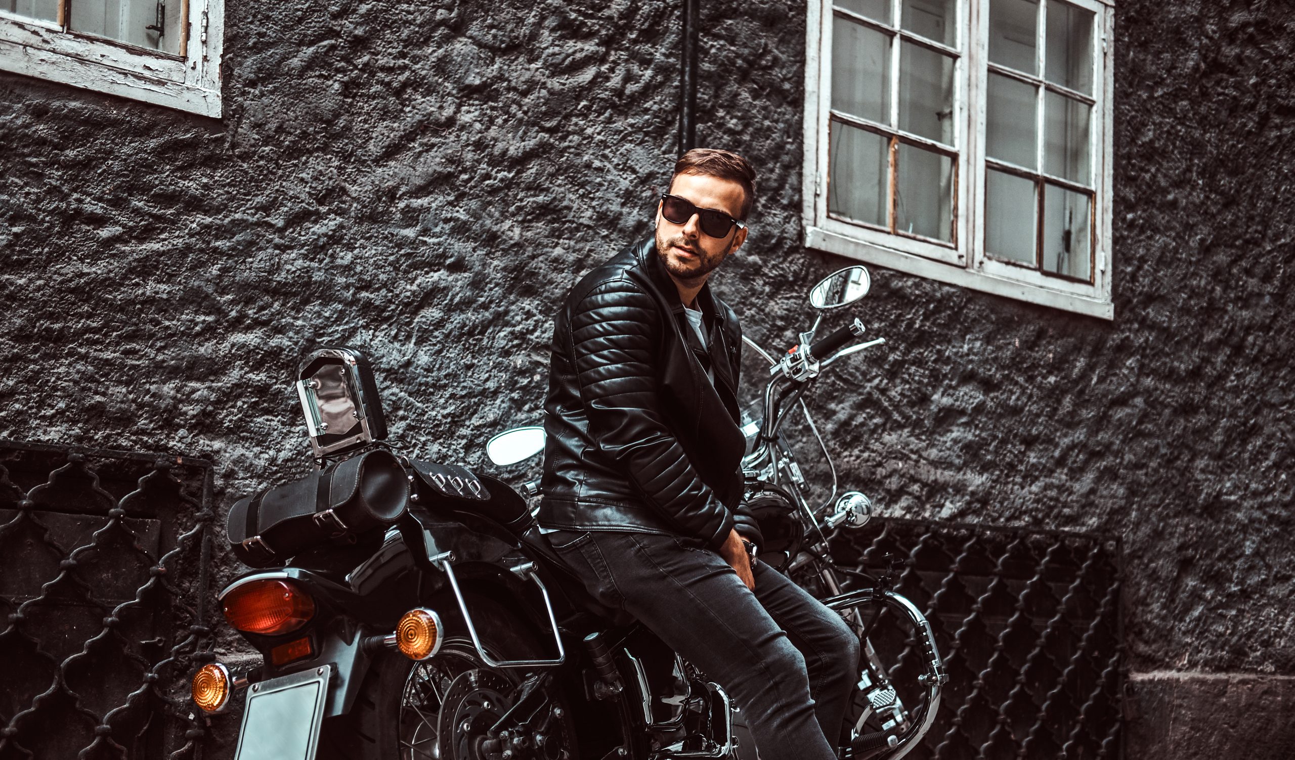Fashionable biker leaning on his retro motorcycle on an old Europe street.